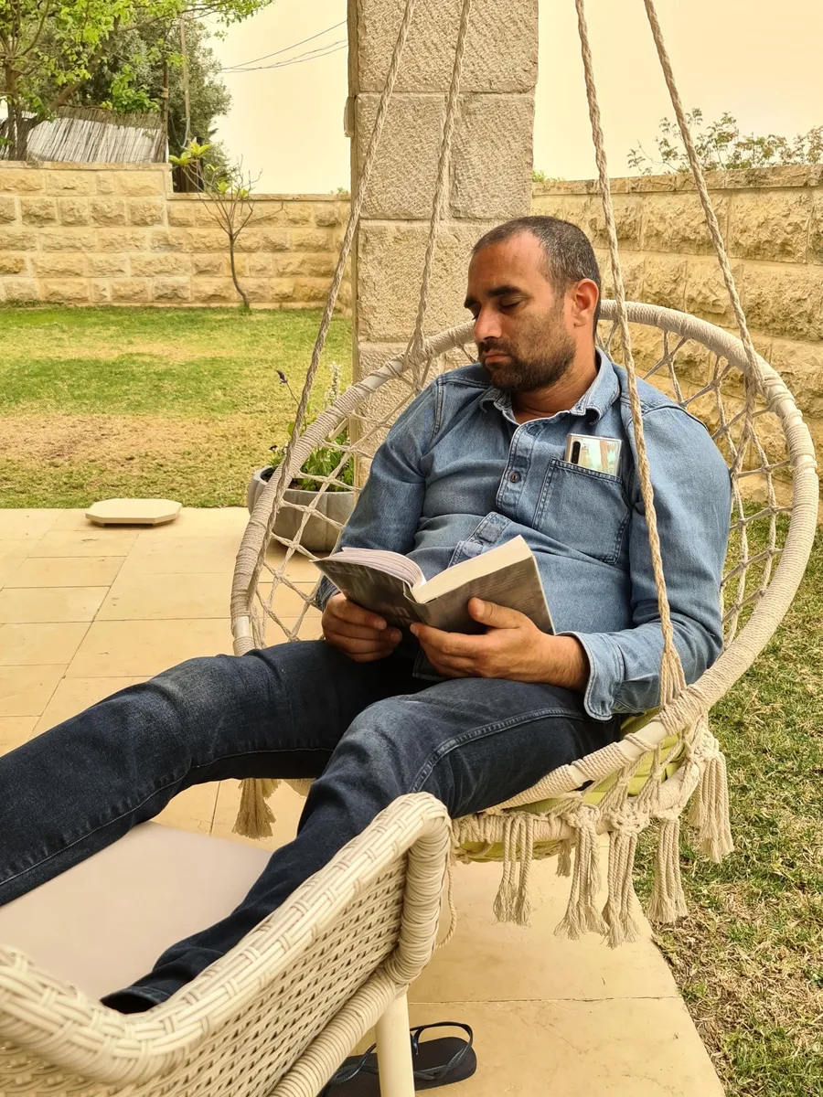איש נח על כיסא נדנדה בחצר עם ספר